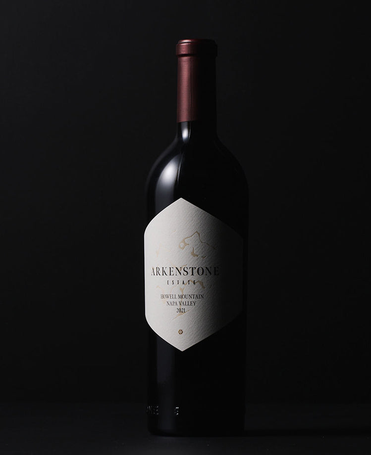 A bottle of Arkenstone Estate 2012 Howell Mountain Napa Valley wine stands upright against a plain black background, with a white label and a maroon foil on the neck.
