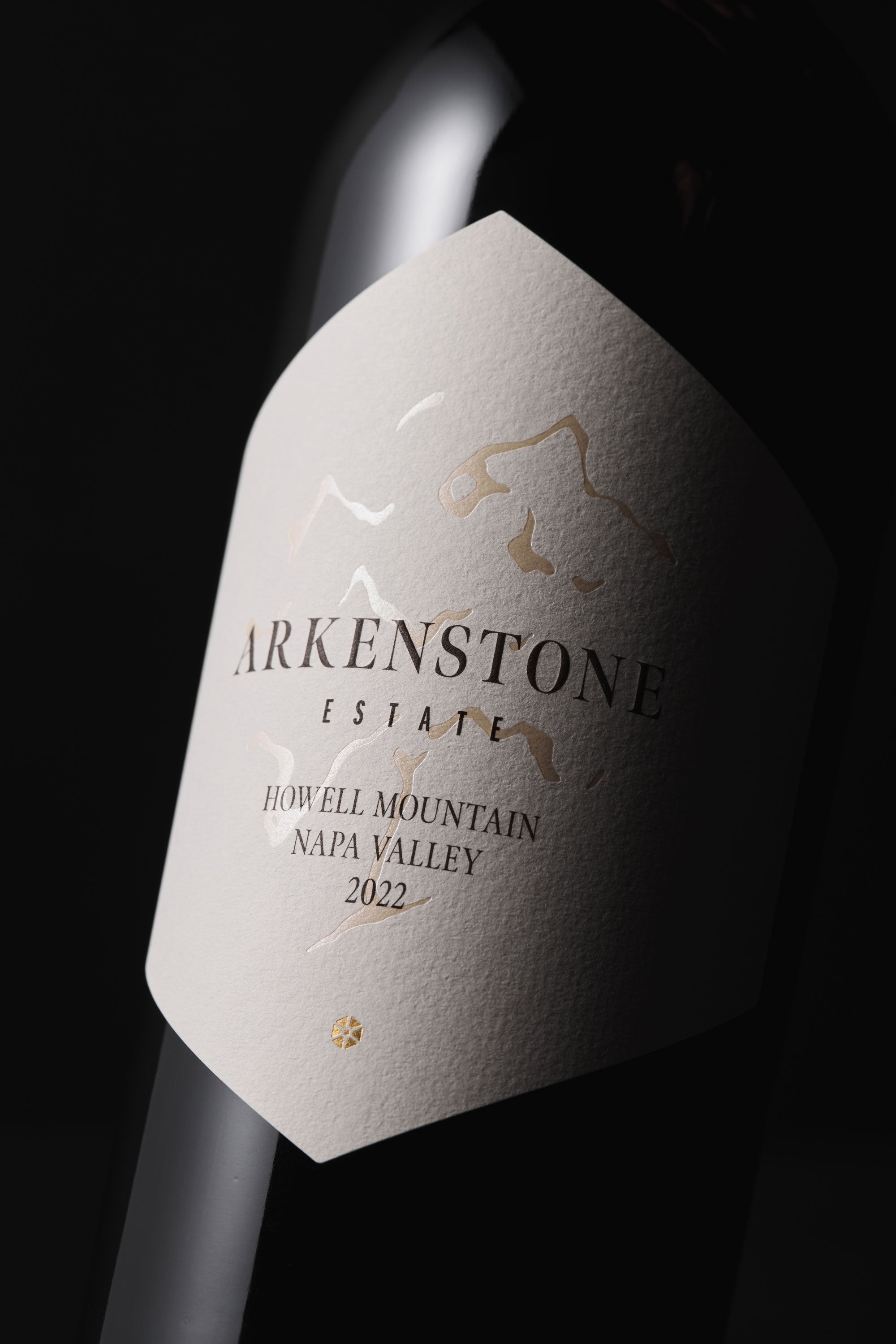 A close-up of a wine bottle with a white label reading Arkenstone Estate, Howell Mountain, Napa Valley, 2022 in black and gold lettering, featuring a subtle embossed mountain design.