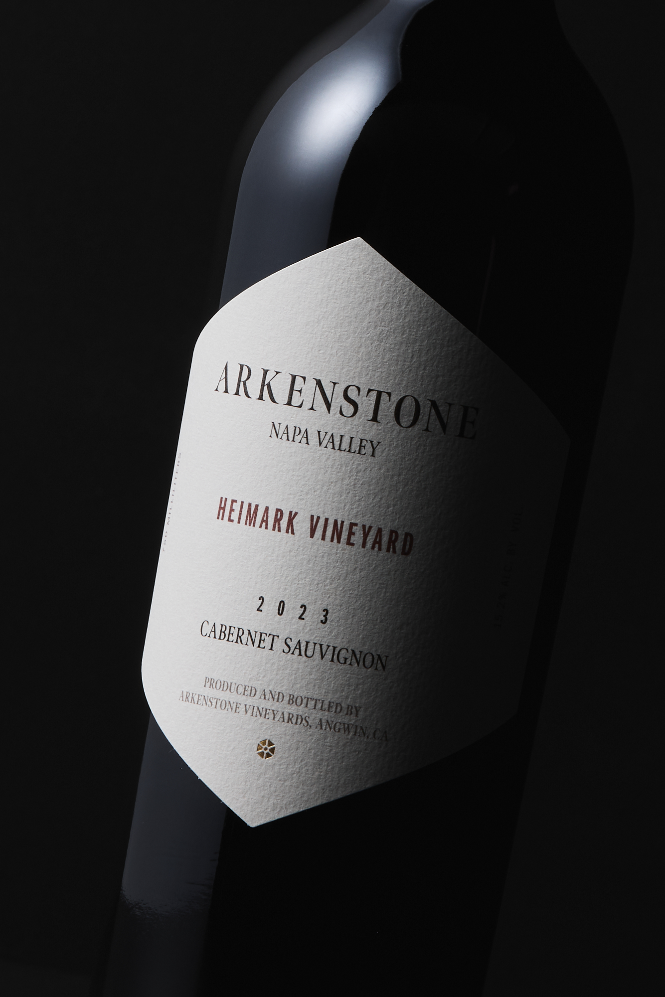 A close-up of a dark wine bottle with a textured white label reading 2023 Heimark Vineyard Cabernet Sauvignon, set against a moody backdrop—an elegant tribute to this distinguished Napa Valley release.