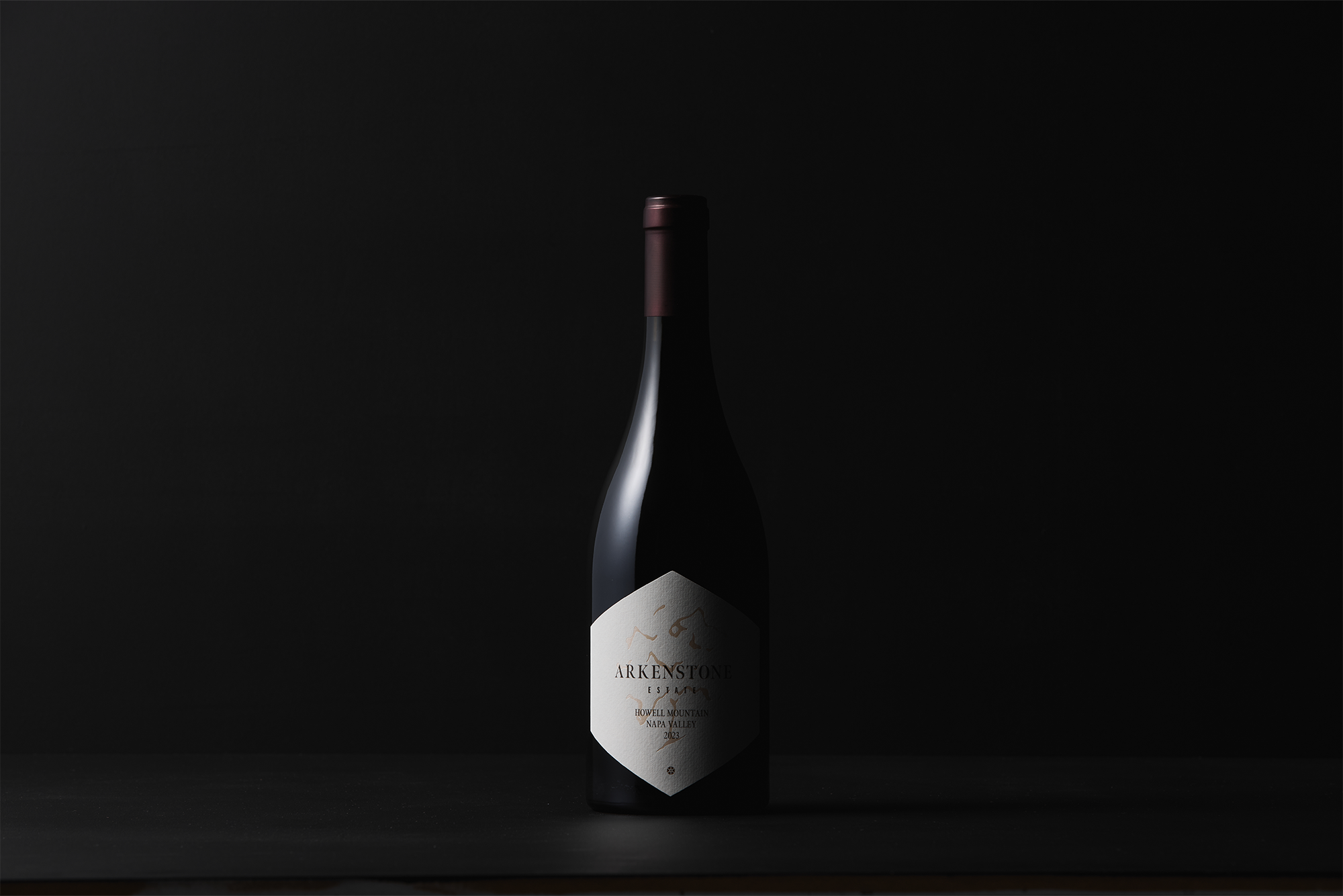 A dark wine bottle with a maroon cap stands against a black background. The label reads 2023 Syrah, hinting at its distinguished origin. Low lighting highlights the elegant shape of the bottle.